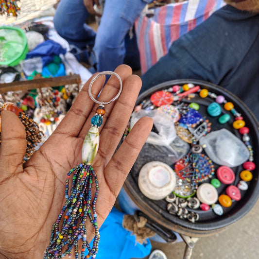Handcrafted beaded tassel keychain with a gray banded agate focal bead and iridescent tassel made in Kibera Kenya.