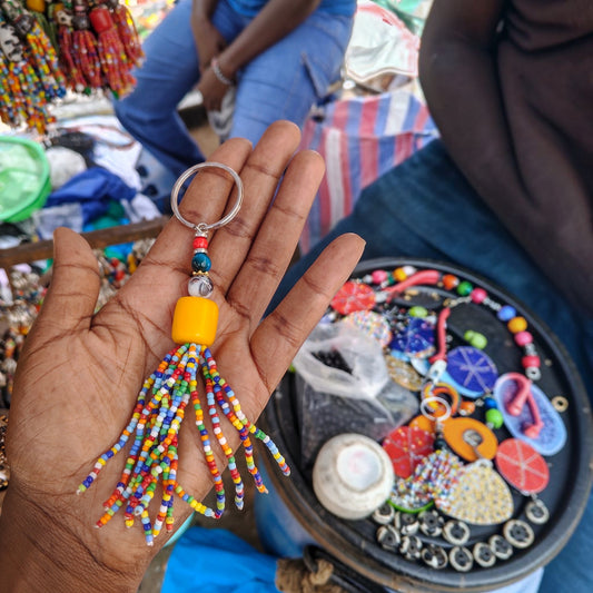 Nualocal handcrafted beaded tassel keychain with multicolored glass seed beads and a yellow focal bead in a hand.