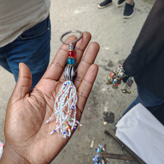 Nualocal handcrafted keychain with a white beaded tassel, amber resin focal bead, and colorful glass accents in a hand.