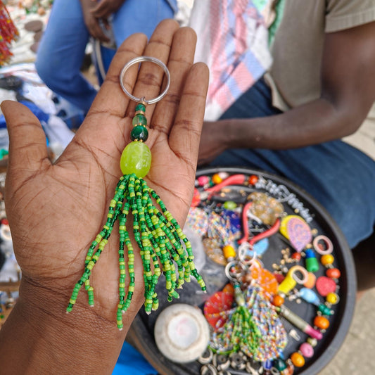 Nualocal handcrafted green glass seed bead tassel keychain with amber resin focal bead held in a person's palm.