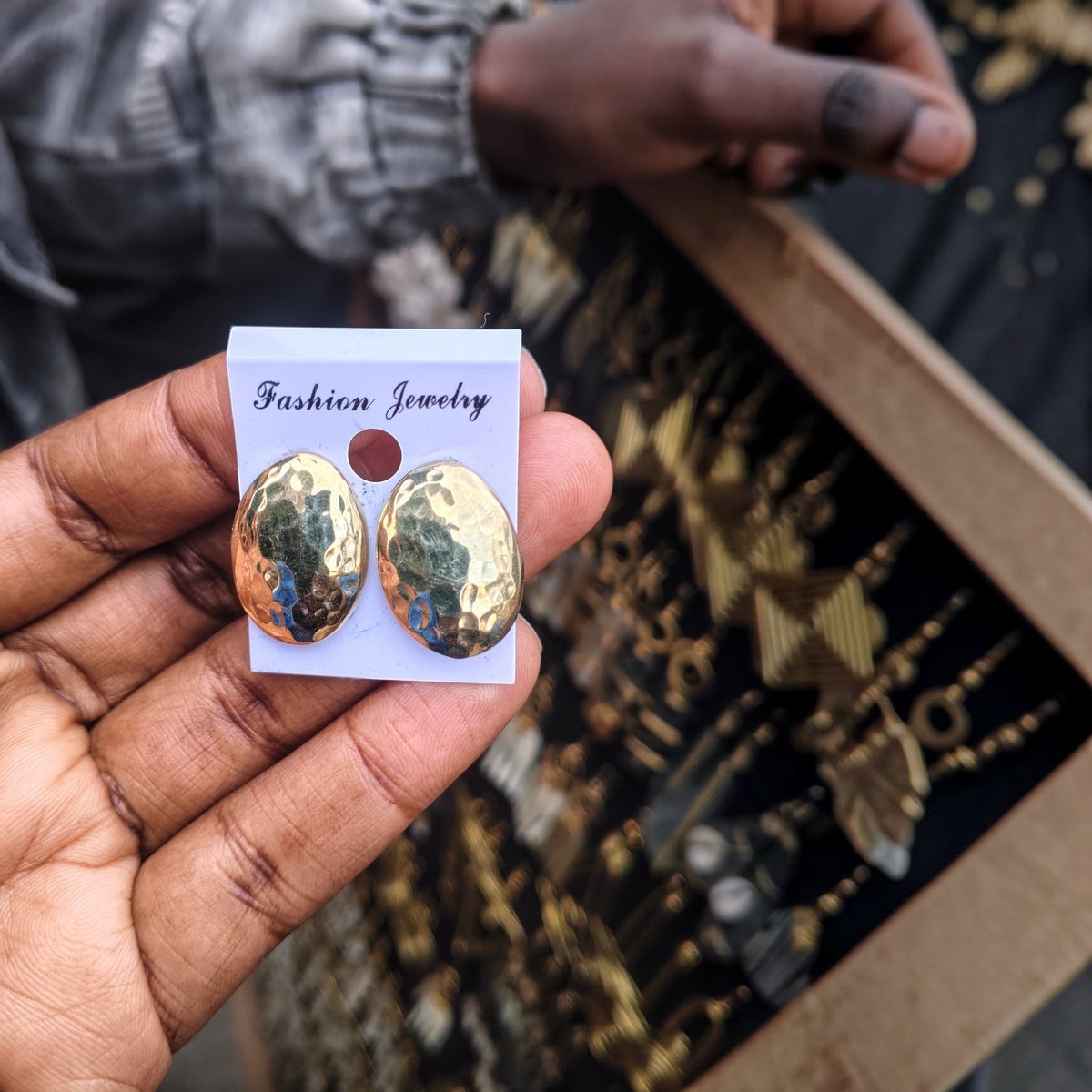 Nualocal hammered oval brass stud earrings held in hand, featuring a textured gold-tone finish and lightweight design.