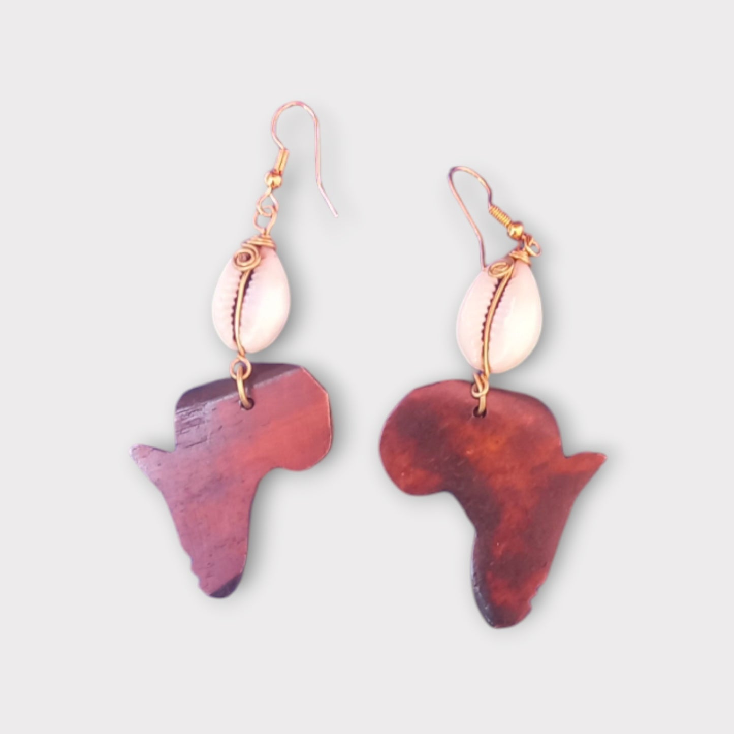 Dangle earrings with a detailed Africa map pendant connected to a small white cowrie shell, made in Kenya.