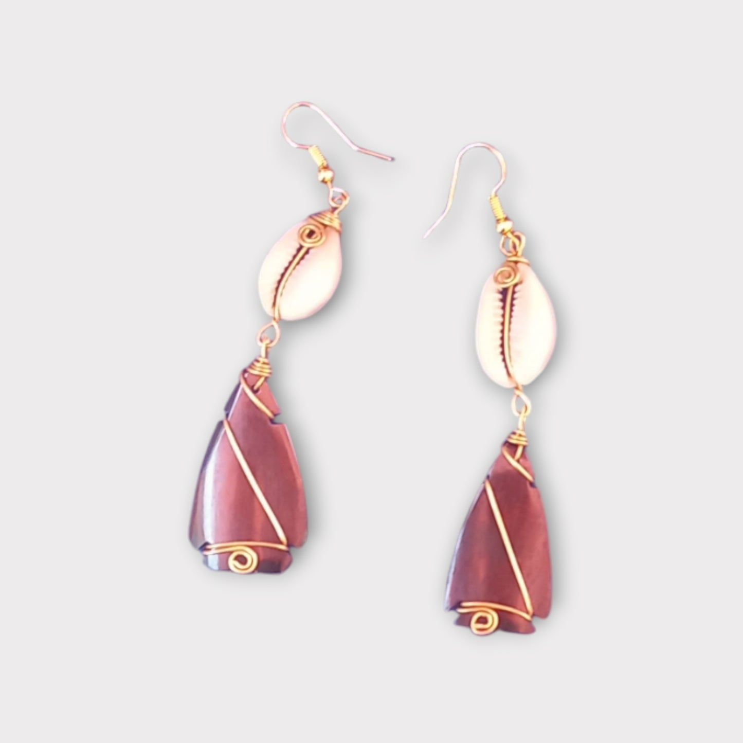 Artisan-crafted earrings from Kenya, showcasing a delicate cowrie shell and a smooth teardrop bone element with detailed gold wire wrapping.