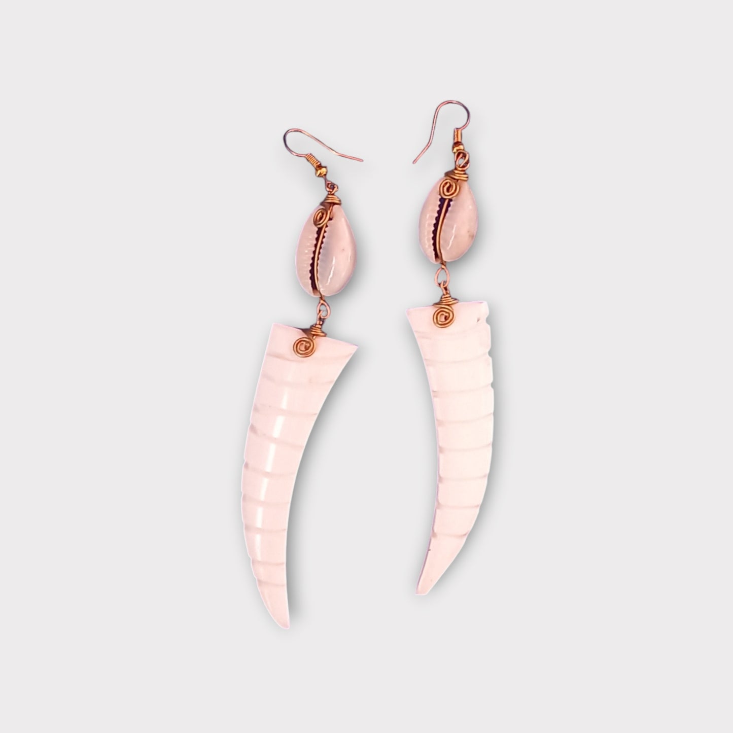Handcrafted Kenyan earrings featuring a white cowrie shell and a curved, tusk-shaped bone pendant with carved ridges.