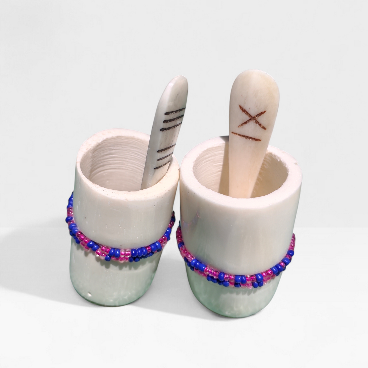 Handcrafted set of 2 tall cylindrical bone spice pots with blue and pink bead bands and etched bone spoons, made in Kibera Nairobi Kenya.