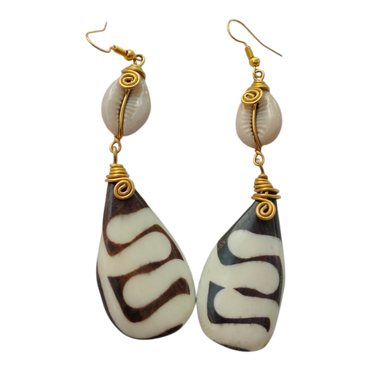 Hand-carved upcycled bone teardrop earrings with brown batik wave pattern, wire-wrapped cowrie shells, and brass coils, made in Kibera, Nairobi, Kenya.