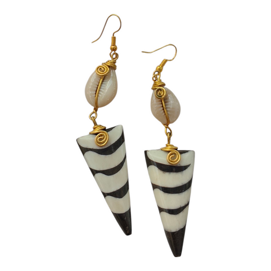 Hand-carved upcycled bone inverted triangle earrings with black and white batik zebra pattern, wire-wrapped cowrie shells, and brass coils, made in Kibera, Nairobi, Kenya.