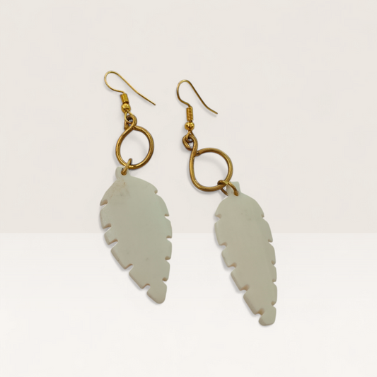 Artisan Kenyan earrings featuring white hand-carved bone leaves suspended from golden brass infinity loops.
