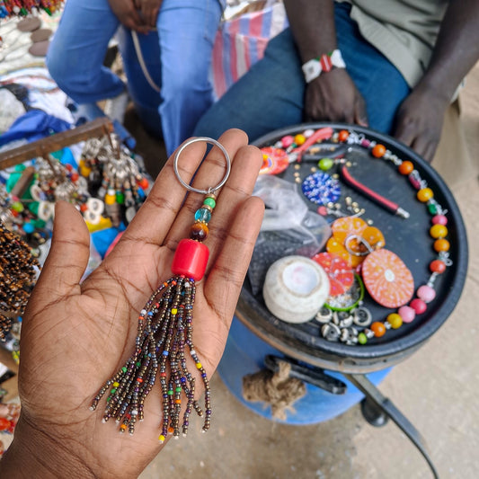 Handcrafted dark metallic beaded tassel keychain with a coral red amber focal bead made by Kibera artisans in Kenya.