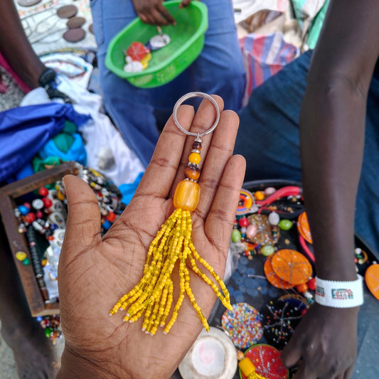 Handcrafted yellow beaded tassel keychain with a honey amber focal bead made in Kibera Kenya.