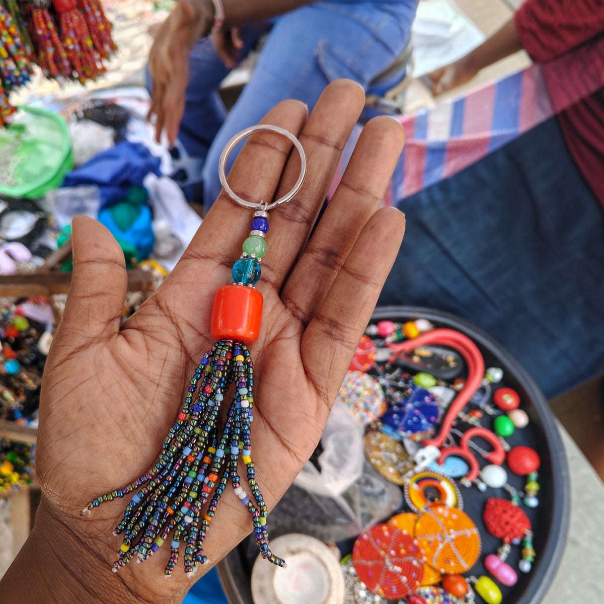 Handcrafted beaded tassel keychain with a bright coral red focal bead and iridescent seed beads made in Kibera Kenya.