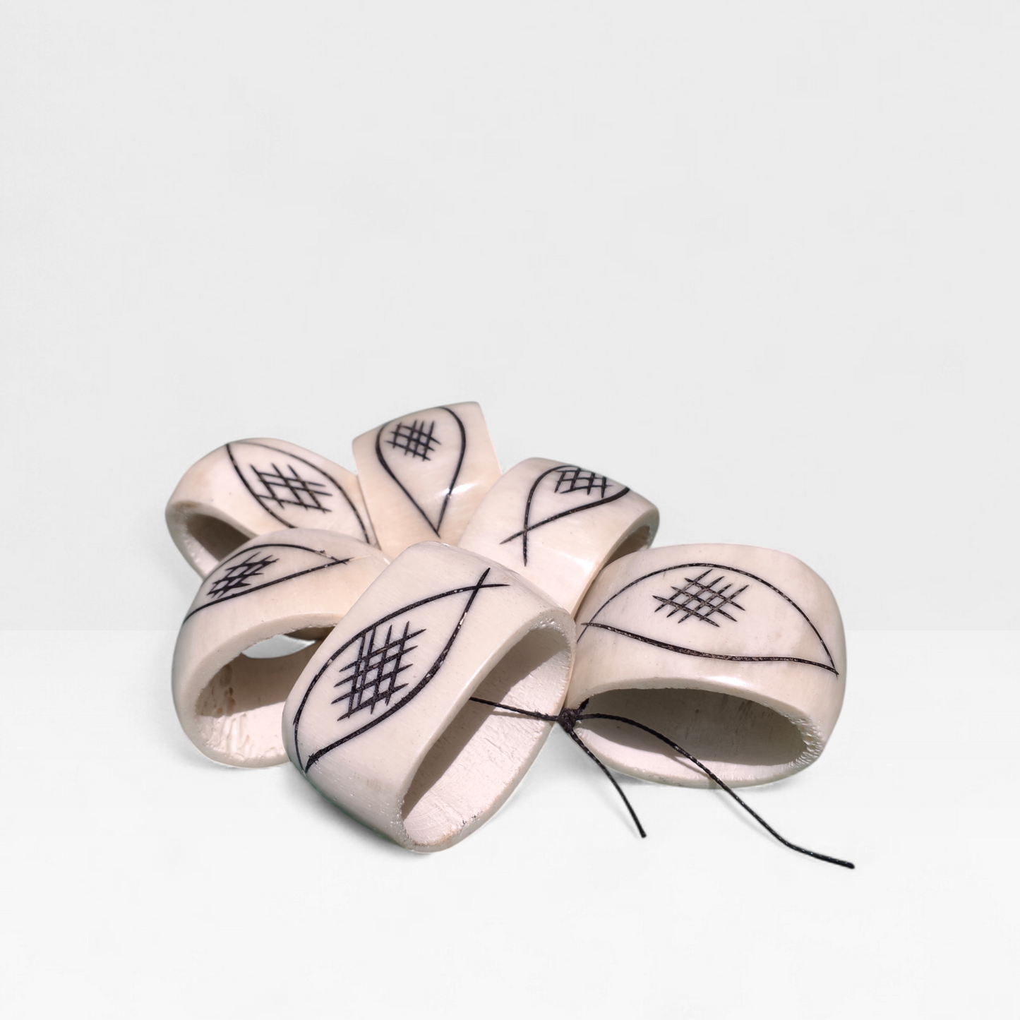 Set of six off-white upcycled cow bone napkin rings hand-etched with a black geometric eye and crosshatch pattern made in Kibera Kenya.