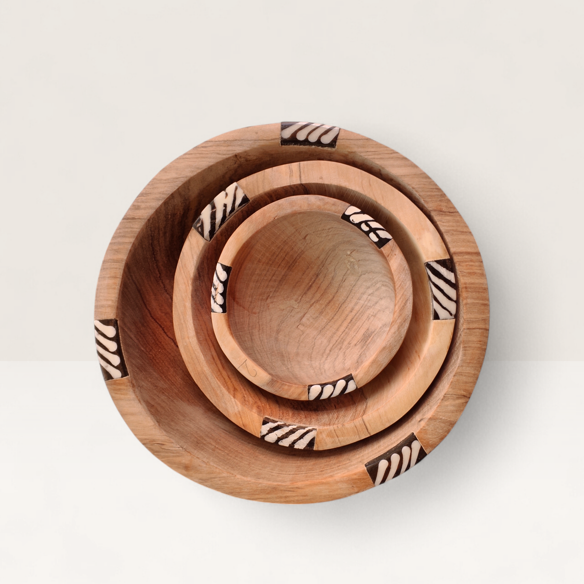 Top-down view of handcrafted 3-piece nesting Kenyan olive wood round bowls with zebra stripe batik bone inlay rim, made in Ukambani Kenya.