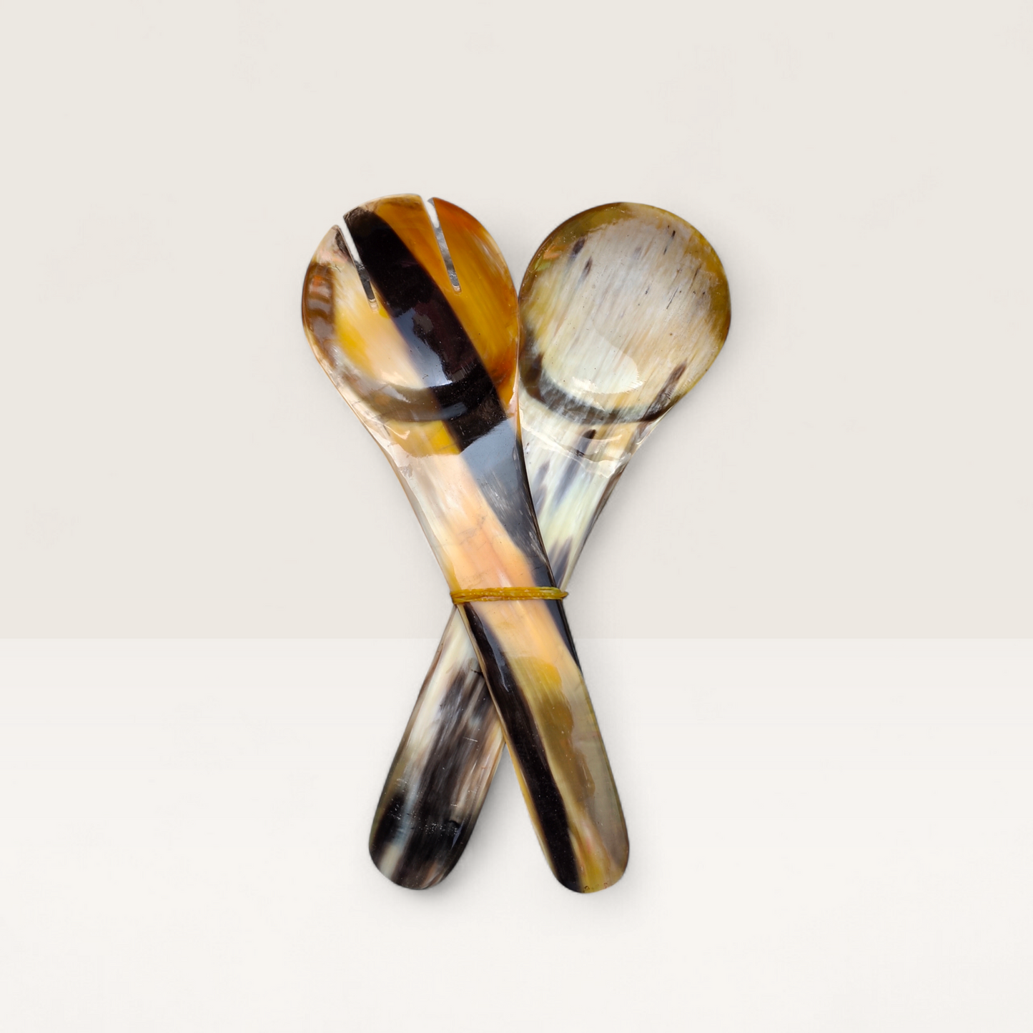 Set of two hand-carved polished cow horn salad serving spoons showcasing natural honey, amber, and dark brown marbled textures, crafted in Kenya.