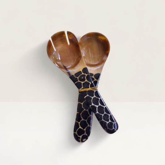 Set of two hand-carved polished cow horn salad serving spoons with natural dark marbling and batik handles, crafted by artisans in Kenya.