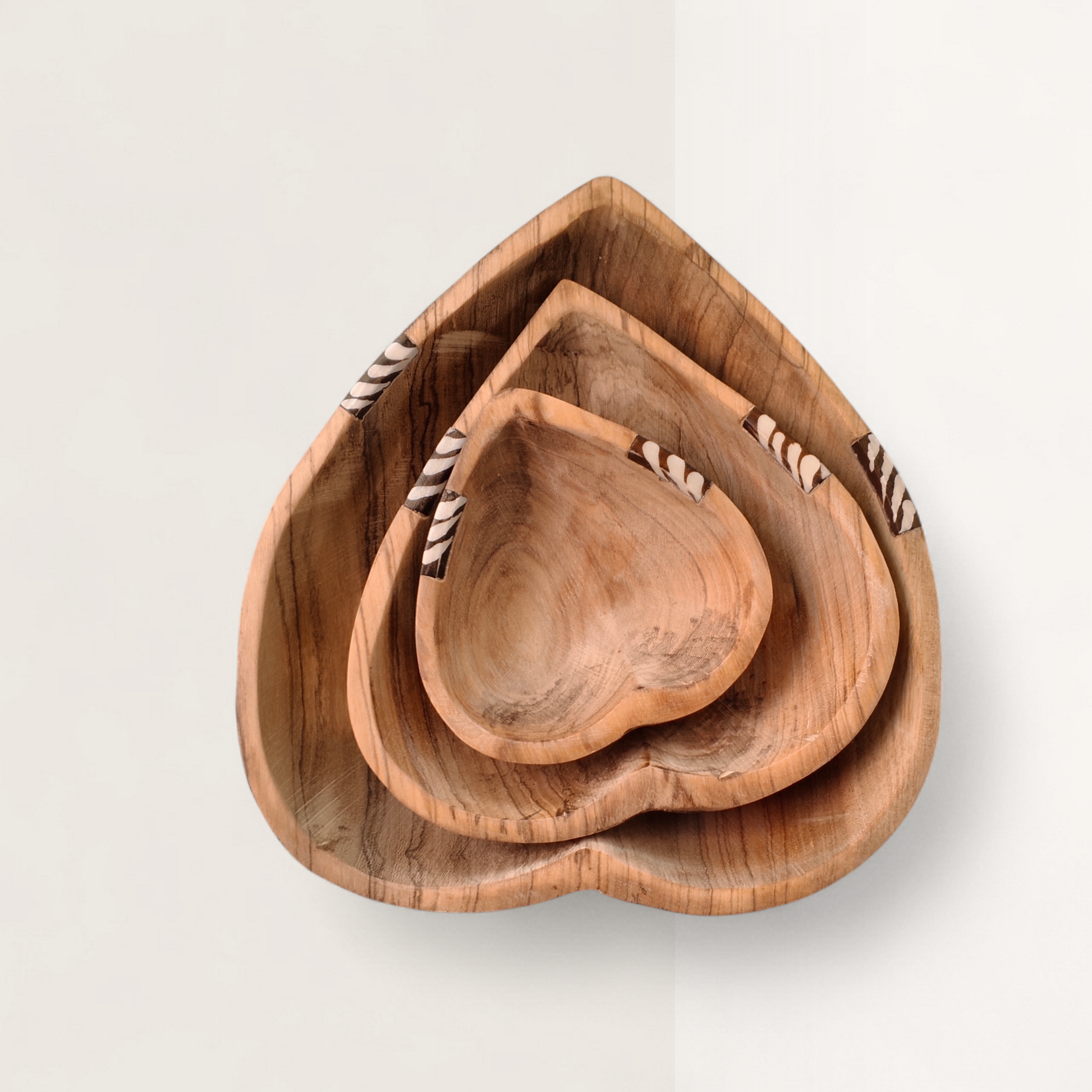 Set of three nesting heart-shaped bowls made of Kenyan olive wood with batik bone inlay on the rims, sizes 8, 6, and 4 inches.