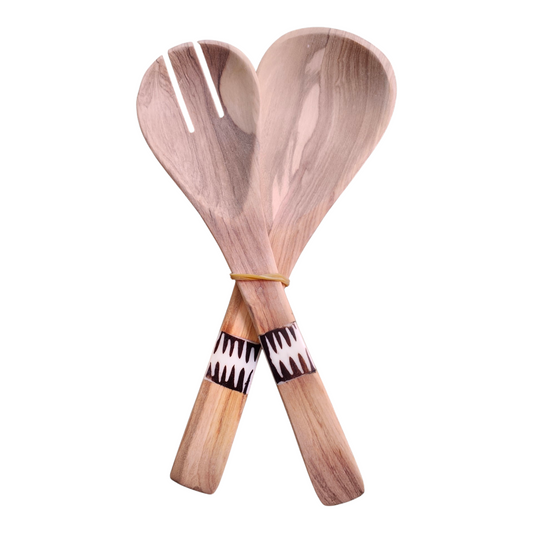 A pair of hand-carved Kenyan olive wood serving spoons with rich honey-toned grain, positioned on a white background