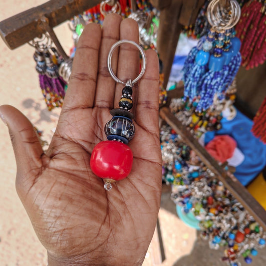 Nualocal handcrafted key holder with red resin amber, batik bone, and glass beads held in a palm in Kenya.