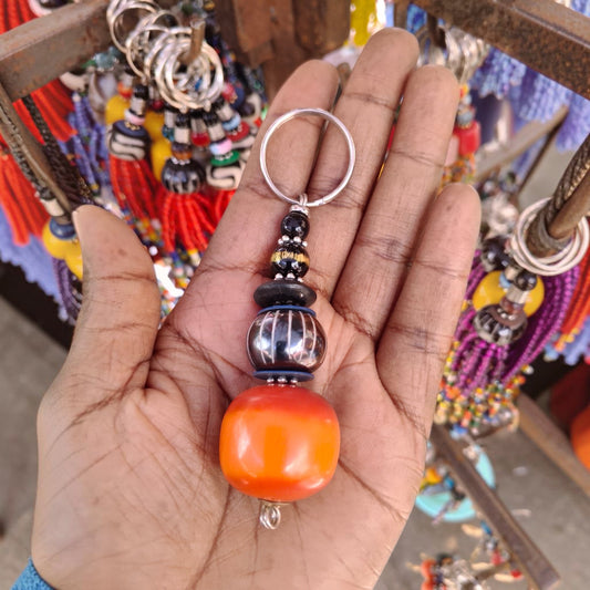 Nualocal handcrafted key holder with amber resin, batik bone, and glass beads held in a palm in Kenya.