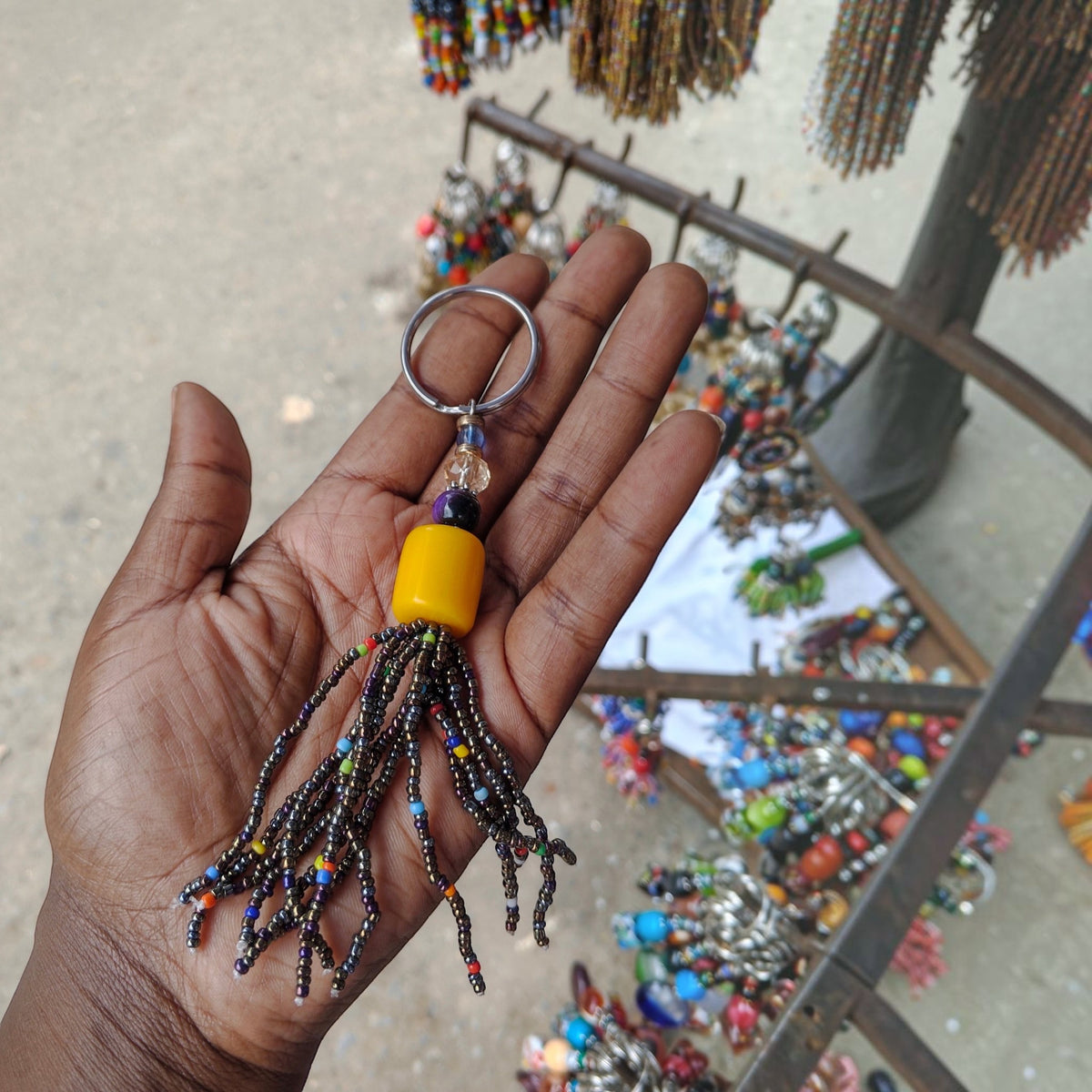 Nualocal handcrafted keychain with a yellow amber resin bead and dark iridescent glass seed bead tassel in a hand
