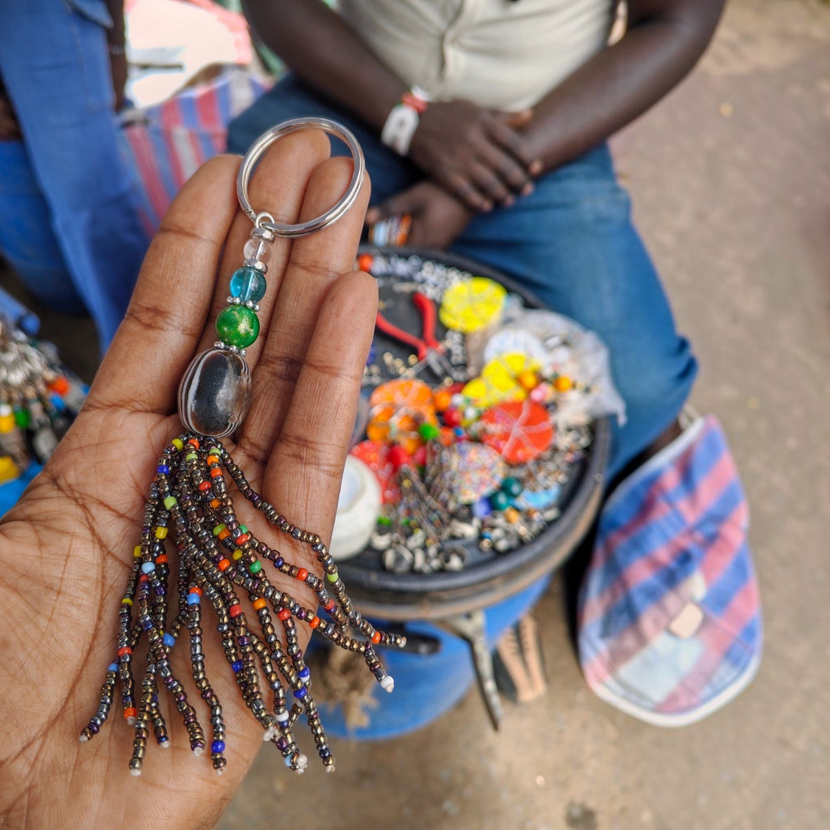 Nualocal handcrafted keychain with amber resin, metallic seed bead tassel, and glass spacers held in a person's hand.
