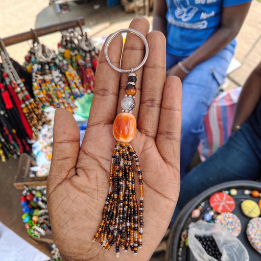 Nualocal handcrafted beaded tassel keychain in amber and earth tones with a metal ring held in a person's palm.
