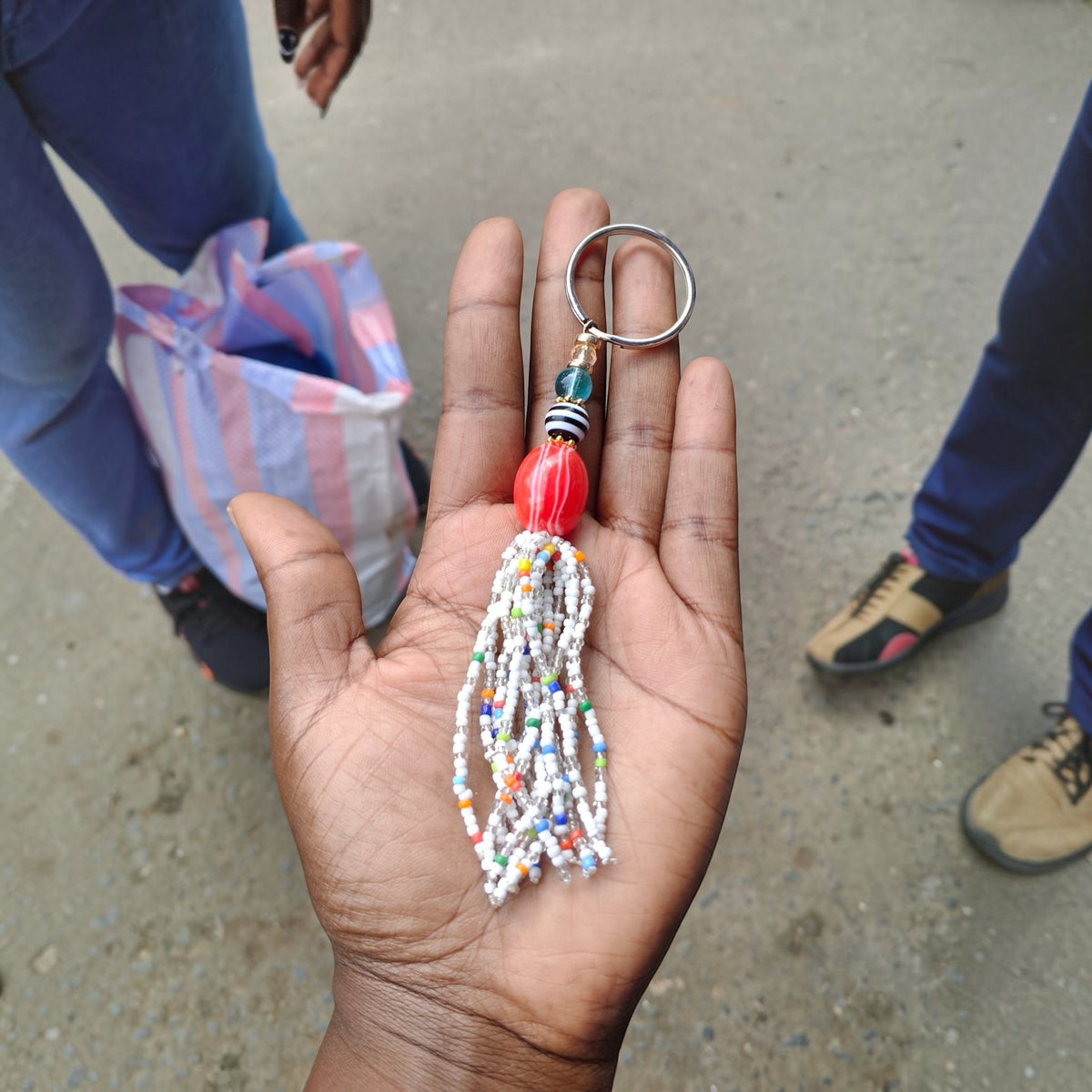 Nualocal handcrafted keychain with white beaded tassel, amber resin bead, and metal ring held in a person's palm.