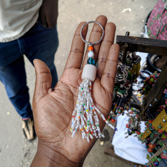 Nualocal handcrafted keychain with a white beaded tassel, amber resin bead, and colorful accents held in a palm.