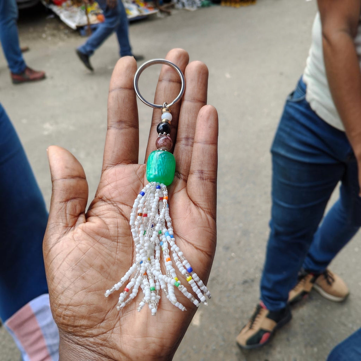 Nualocal handcrafted keychain with white glass bead tassel, green resin bead, and metal ring held in a palm.