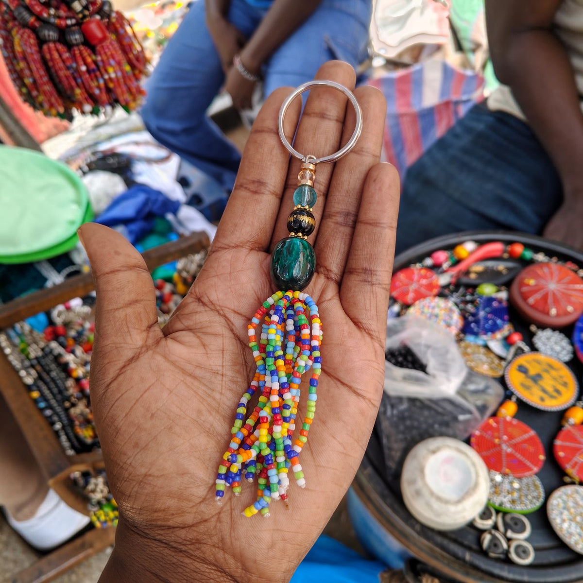 Nualocal handcrafted multicolored glass seed bead tassel keychain with a polished focal bead held in a palm.