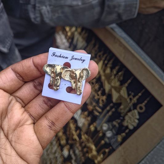 Nualocal handcrafted brass elephant head stud earrings with detailed textures held in a hand.