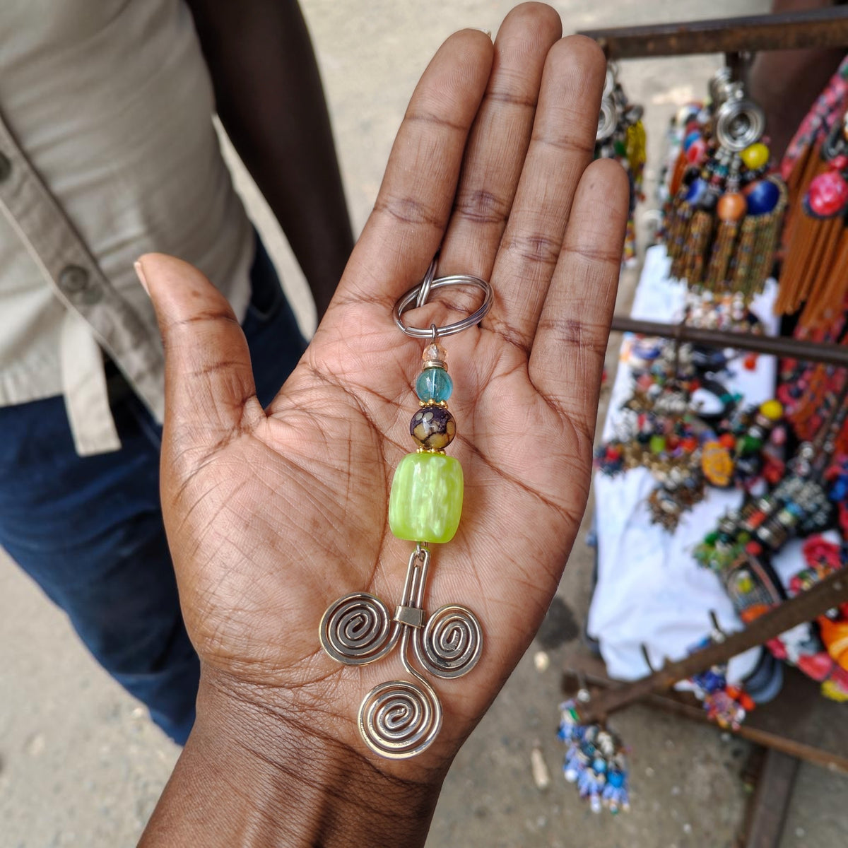 Nualocal handcrafted key holder with brass triple-spiral motif, lime green resin bead, and blue glass accents.