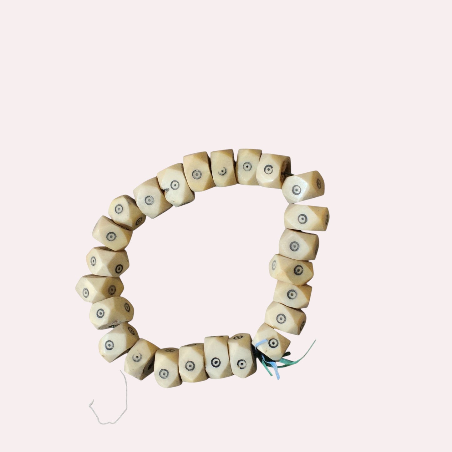Nualocal hand-carved geometric bone beads from Kenya featuring black batik dot-in-circle eye motifs on a white strand.