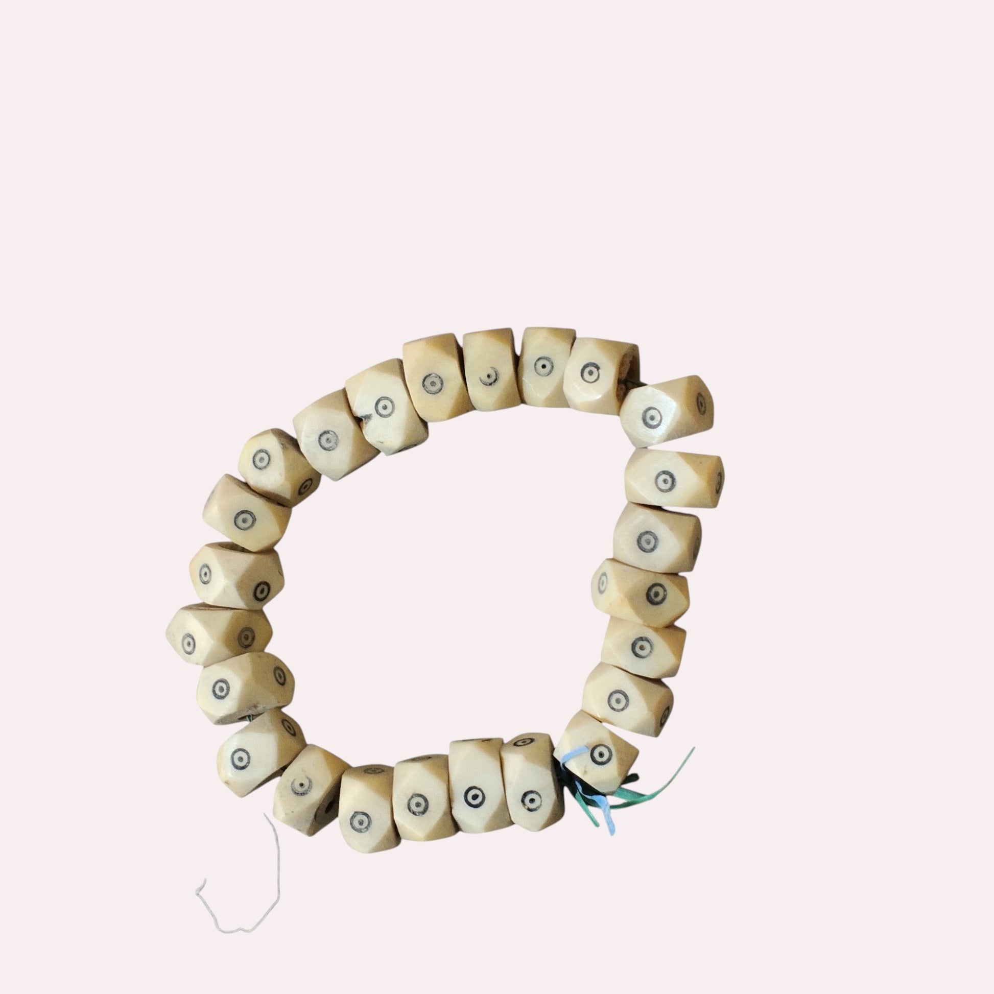 Nualocal hand-carved geometric bone beads from Kenya featuring black batik dot-in-circle eye motifs on a white strand.