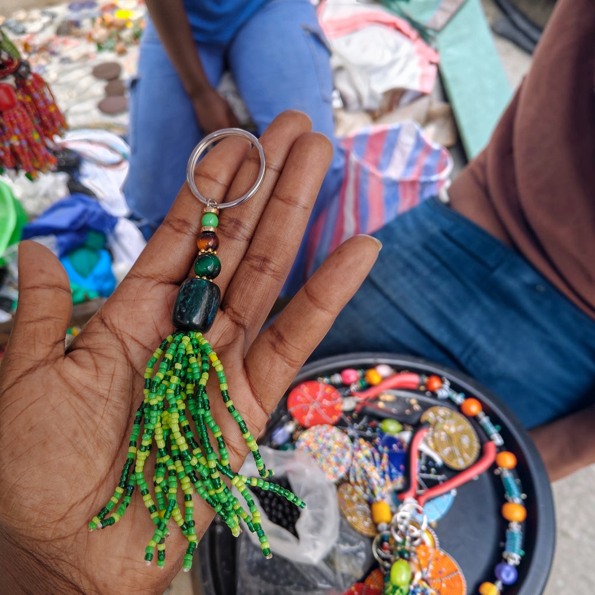 Nualocal handcrafted green glass seed bead tassel keychain with amber resin focal bead held in a person's hand.