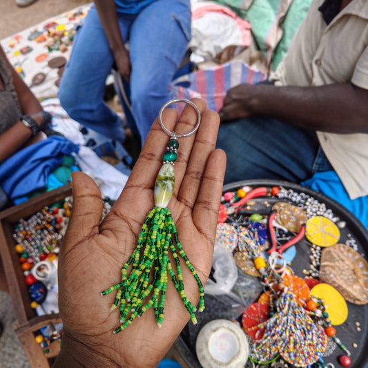 Nualocal handcrafted green glass bead tassel keychain with amber-style resin focal bead held in a person's palm.