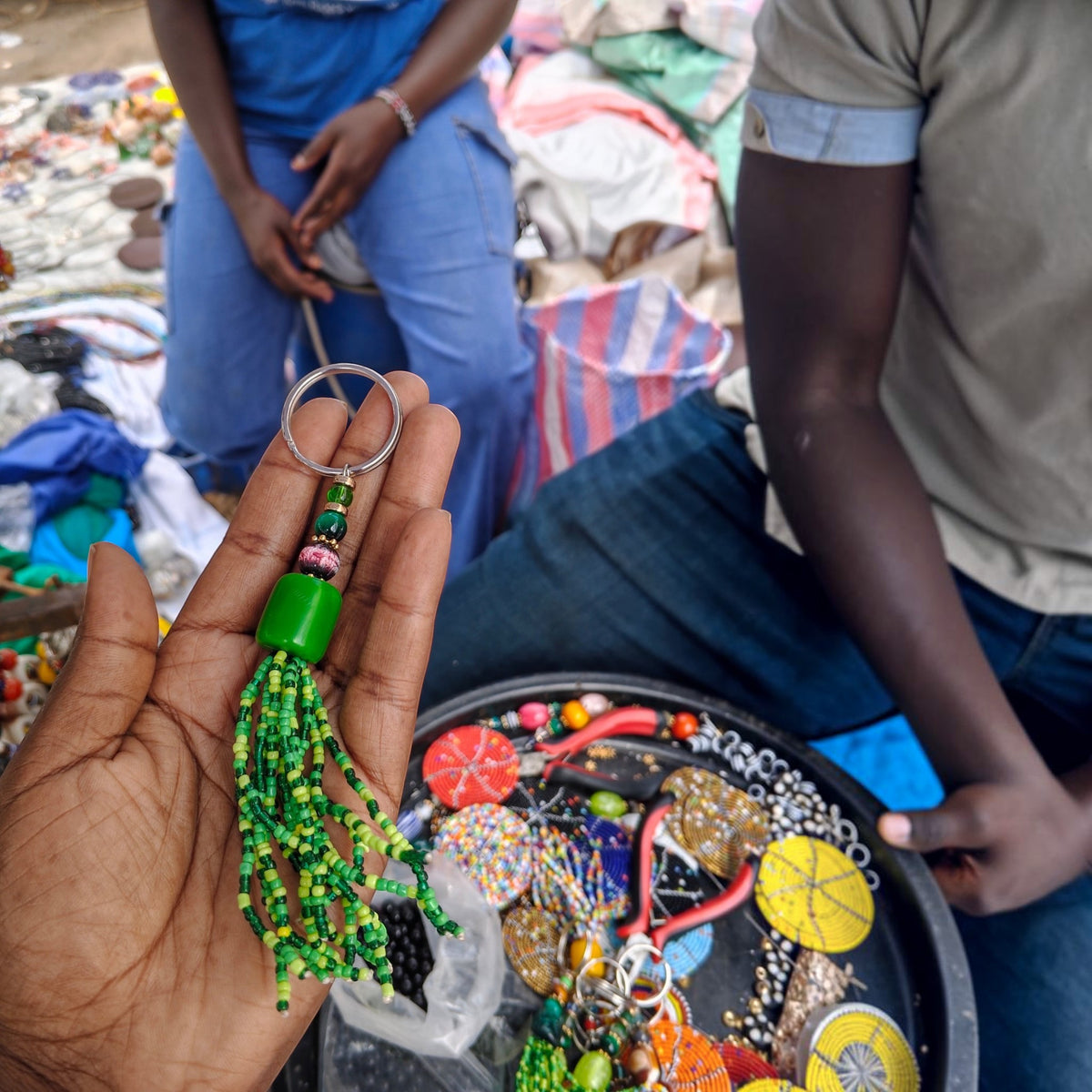 Nualocal handcrafted green glass seed bead tassel keychain with amber-style resin beads held in a person's hand.