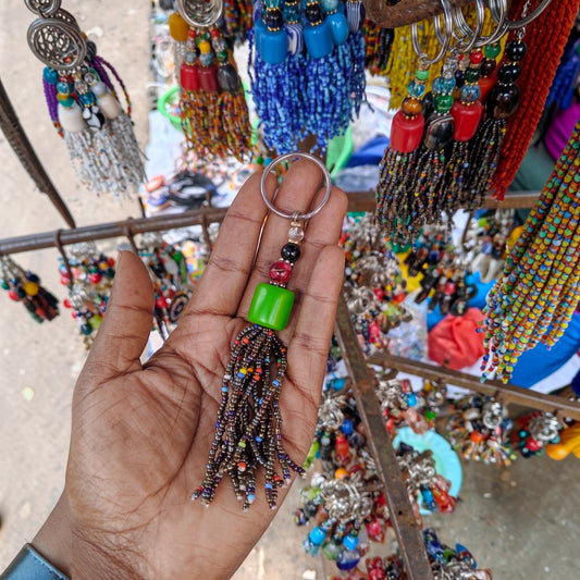 Nualocal handcrafted keychain with a green resin bead, metallic seed bead tassel, and metal ring held in a hand.