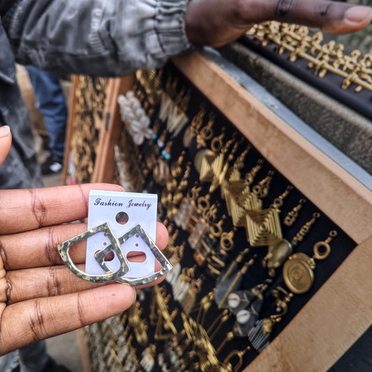 Nualocal brass fan hoop earrings with a hammered texture held in a hand at an artisan market in Kibera, Kenya.