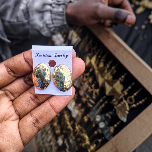 Nualocal hammered oval brass stud earrings held in hand, featuring a textured gold-tone finish and lightweight design.