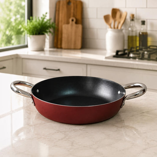 Nualocal Kaluworks maroon non-stick aluminium paella pan with stainless steel loop handles on a kitchen countertop.