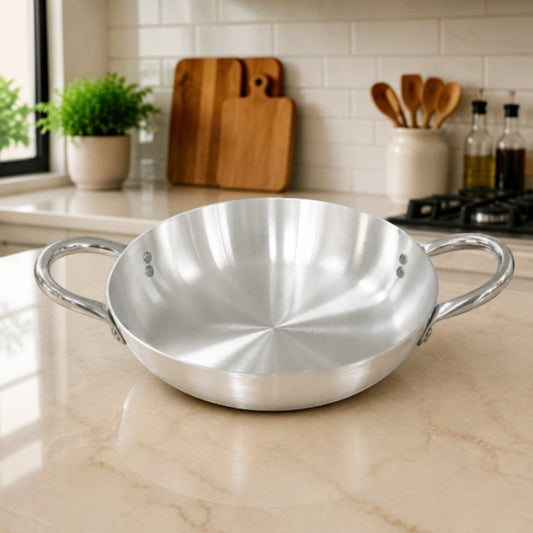 Nualocal Pardini 701 Series polished aluminium paella pan with stainless steel loop handles on a kitchen countertop.