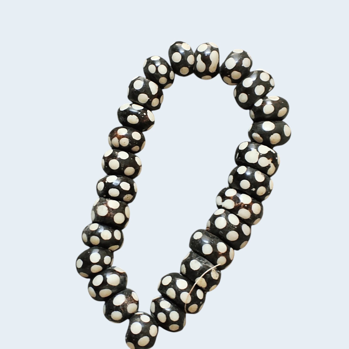 Nualocal hand-carved bone beads with black and ivory polka dot batik patterns, arranged in a circular strand.