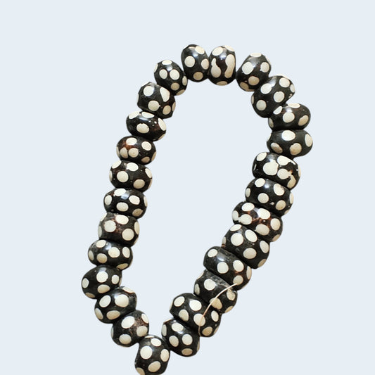 Nualocal hand-carved bone beads with black and ivory polka dot batik patterns, arranged in a circular strand.