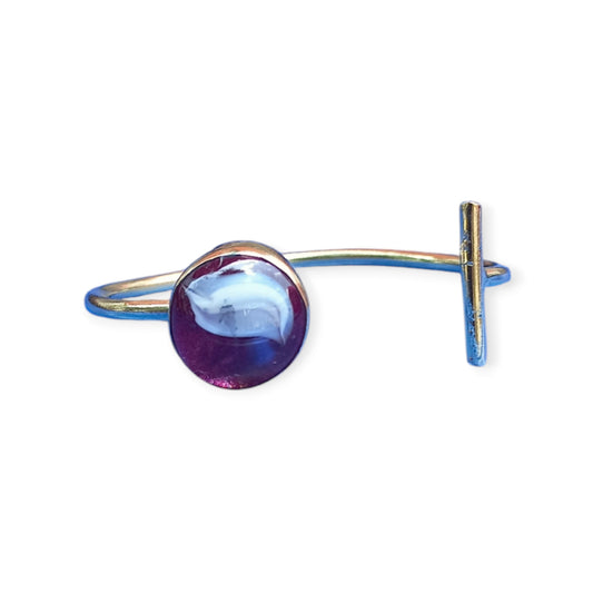 A handcrafted, adjustable brass bracelet from Kenya, designed as an open cuff and featuring a prominent amber ornament with swirling purple, white hues.