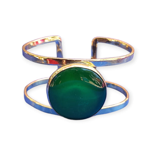 A handcrafted, adjustable brass bracelet from Kenya, designed as a double open cuff and featuring a striking, large emerald green amber ornament.