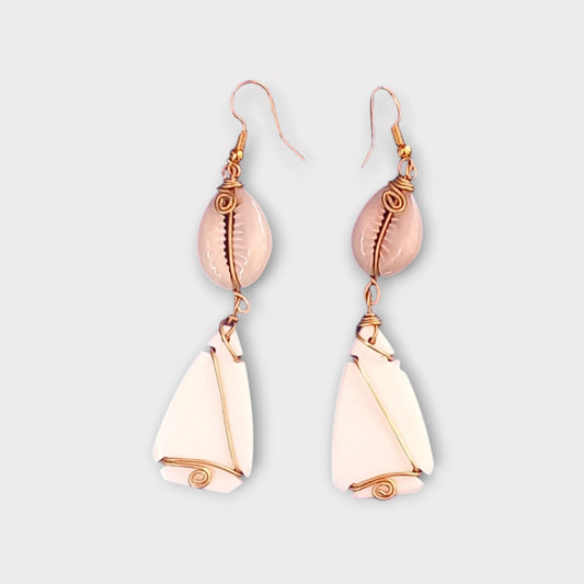 Modern coastal dangle earrings with a small white cowrie shell connected to an abstract, curved bone piece with intricate gold wire wrapping, made in Kenya.