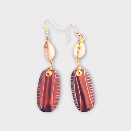A pair of unique dangle earrings made in Kenya, featuring a white cowrie shell and a smooth, striped oval bone.
