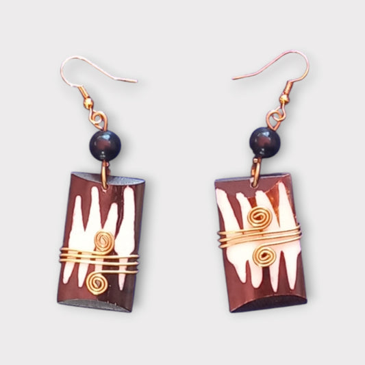 A pair of striking dangle earrings made in Kenya, featuring a rectangular bone with a tribal-inspired pattern, wrapped in brass, and with a dark bead accent.